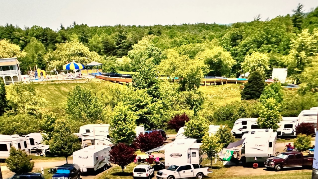 A vibrant, sun-drenched RV site near Azle featuring various white travel trailers and pickup trucks parked in designated spots, illustrating the difference between premium short-term sites and established long-term RV parking areas.