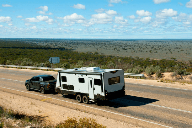 A dark pickup truck towing a modern white travel trailer along a vast desert highway under a bright blue sky, illustrating the freedom of mobile living and the need for reliable wireless internet for RV travel while on the move.